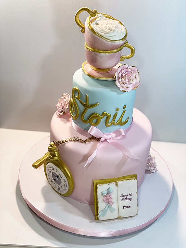 Alice in Wonderland 1st birthday cake with stacked teacups, a pocket watch and a storybook