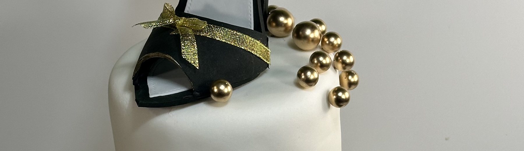 White cake topped with a black and gold sugar stiletto and gold pearls