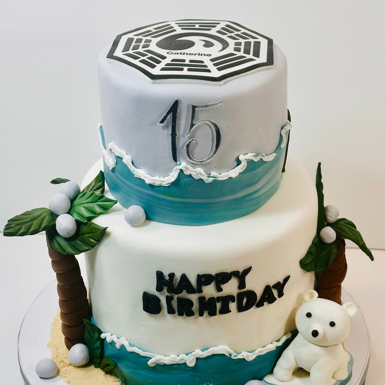Two-tier Lost TV show 15th birthday cake with the Dharma logo, palm trees and a fondant polar bear