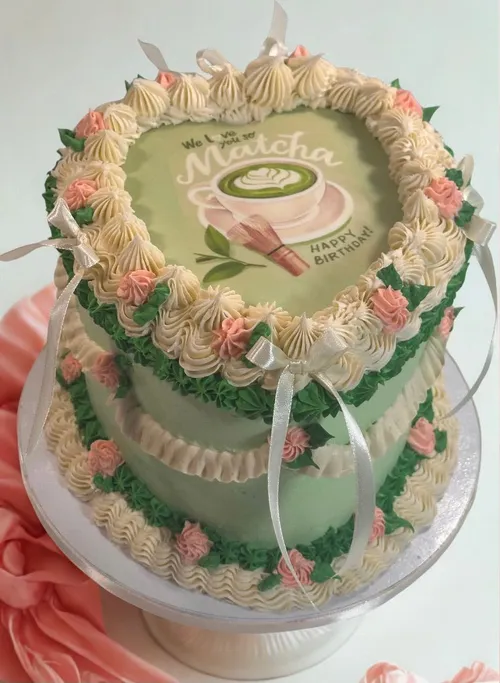 Heart-shaped green matcha cake with piped pink and cream rosettes and ribbon