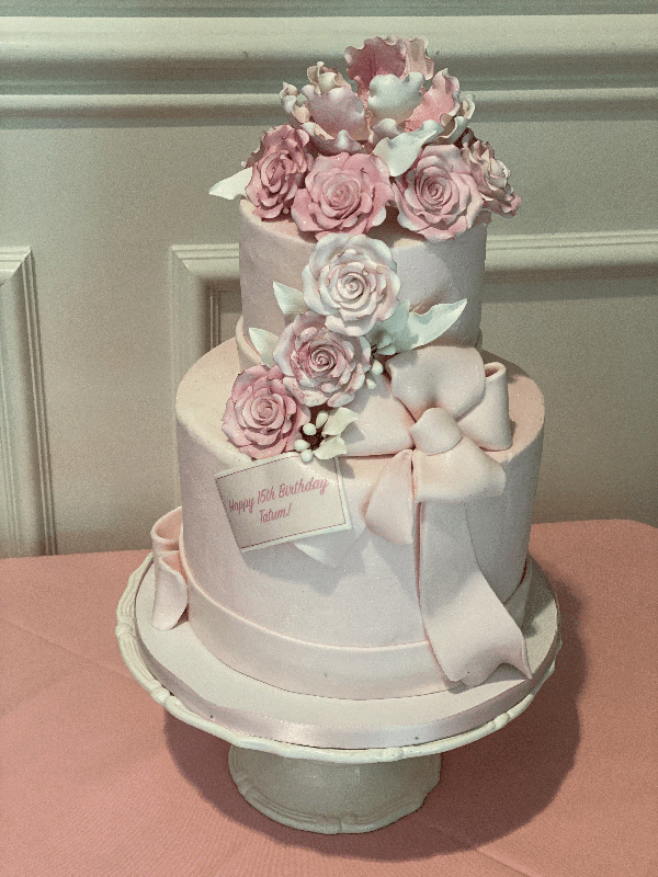 Two-tier blush pink birthday cake with cascading pink sugar roses and a fondant bow