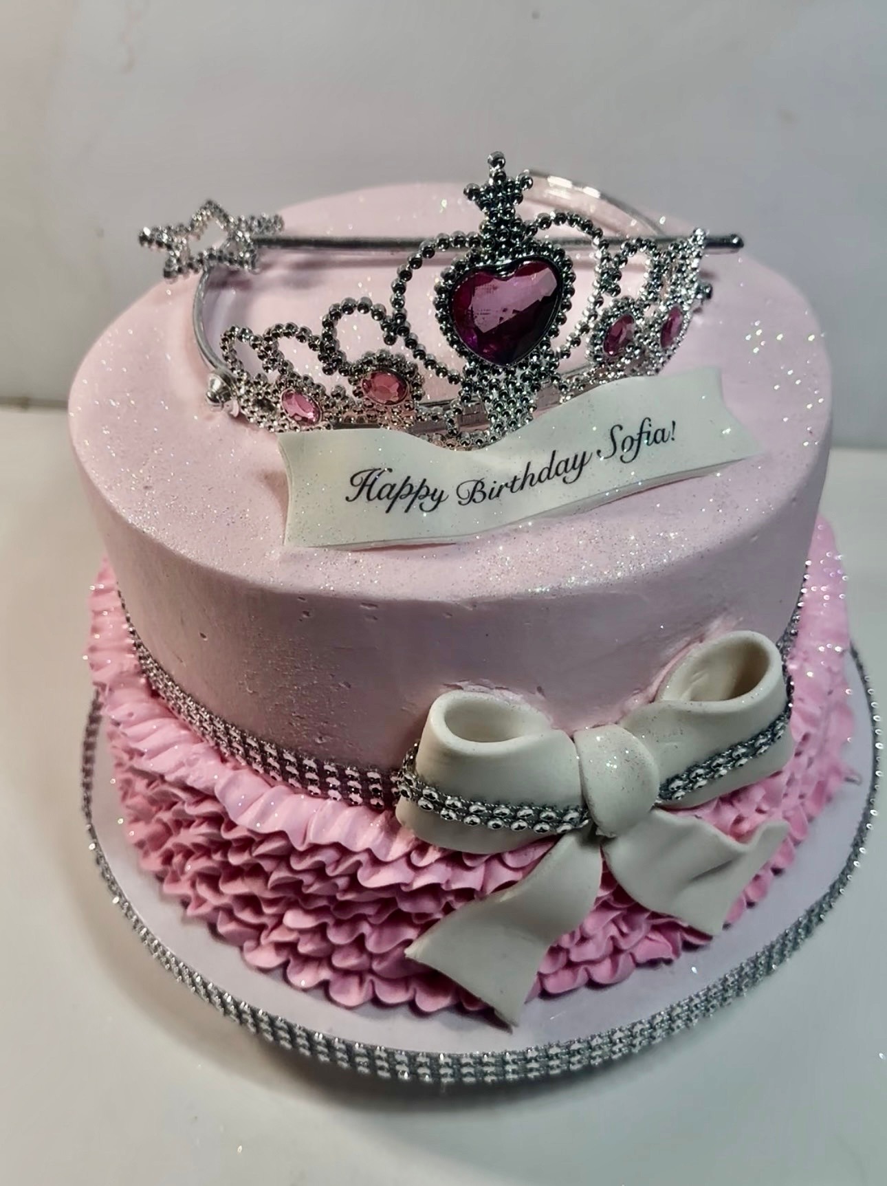 Pink princess birthday cake with a jeweled tiara, pink ruffles and a fondant bow