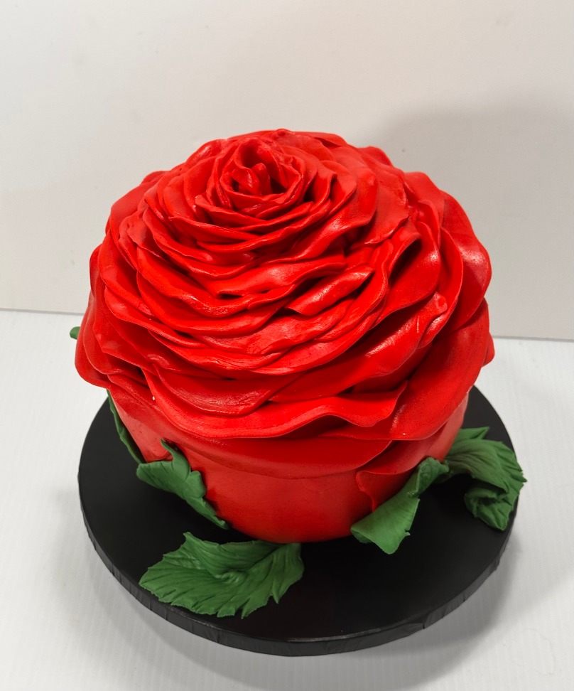 Sculpted red rose cake with green fondant leaves on a black board