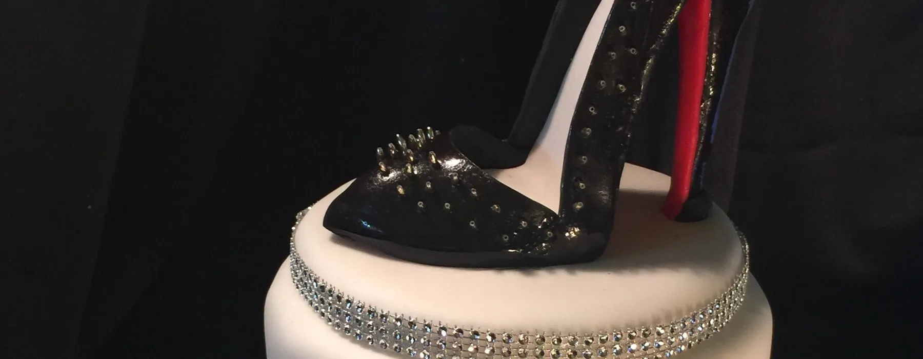 Sculpted black studded stiletto heel on a white cake with a rhinestone band