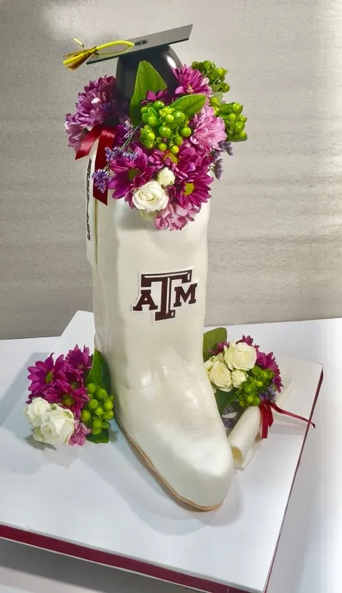 Sculpted white Texas A&M boot graduation cake filled with purple and green flowers